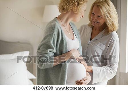 Smiling mother touching pregnant daughter's stomach View Large Photo Image Stock Photo - Smiling mother touching pregnant daughter's stomach. Fotosearch
