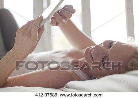 Smiling woman laying in bed and using digital tablet View Large Photo Image Stock Photo - Smiling woman laying in bed and using digital tablet. Fotosearch