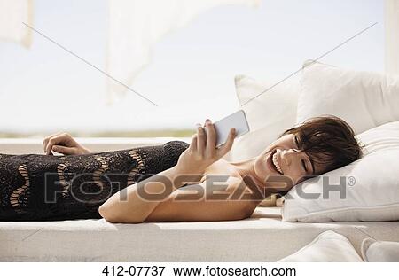Smiling woman text messaging with cell phone on patio sofa View Large Photo Image Stock Photo - Smiling woman text messaging with cell phone on patio sofa. Fotosearch