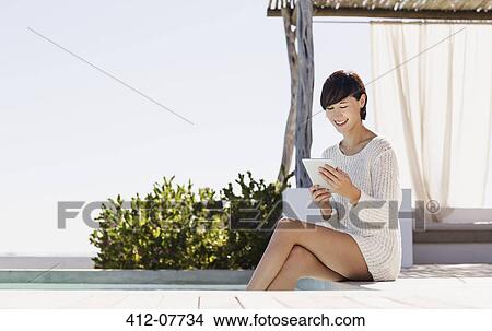 Picture - Smiling woman using digital tablet at poolside. Fotosearch