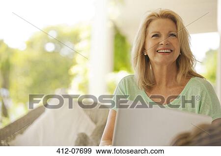 Stock Photo - Smiling woman using laptop on patio. Fotosearch