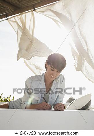 Stock Image - Smiling woman writing on sunny patio. Fotosearch