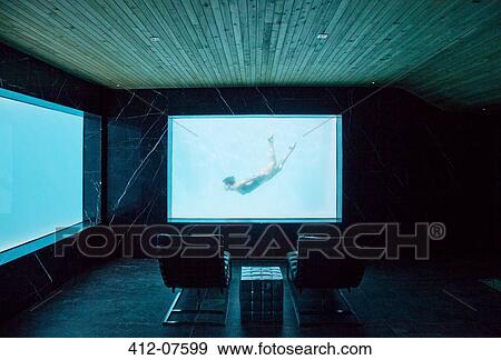 Stock Photo - View of woman swimming underwater from window in pool room. Fotosearch