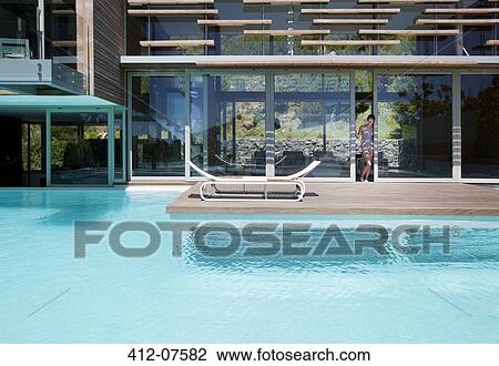 Stock Image - Woman at doorway of patio and swimming pool. Fotosearch