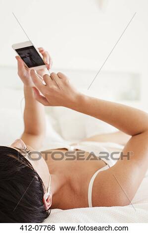 Woman laying in bed using cell phone View Large Photo Image Stock Photograph - Woman laying in bed using cell phone. Fotosearch