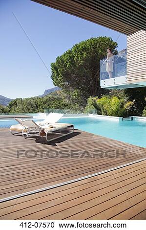 Stock Image - Woman on balcony above swimming pool. Fotosearch