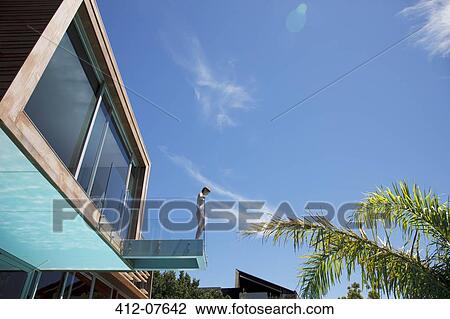 Stock Image - Woman standing at the edge of modern balcony. Fotosearch