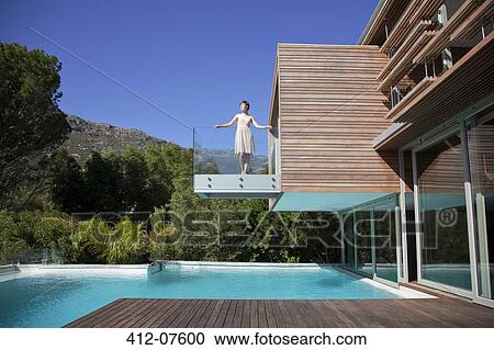 Stock Image - Woman standing on balcony over swimming pool. Fotosearch