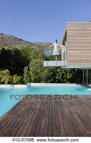 Stock Photo - Woman standing on luxury balcony over swimming pool. Fotosearch