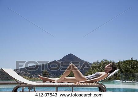 Stock Image - Woman sunbathing lounge chair poolside. Fotosearch