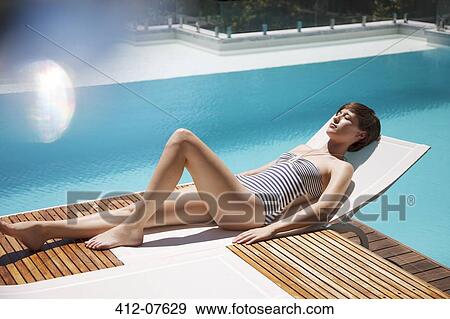Woman Sunbathing On Lounge Chair At Luxury Poolside Stock Photo