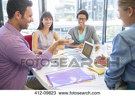 Stock Image - Business people examining ball in office. Fotosearch