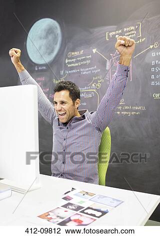 Businessman cheering at desk in office View Large Photo Image Stock Image - Businessman cheering at desk in office. Fotosearch