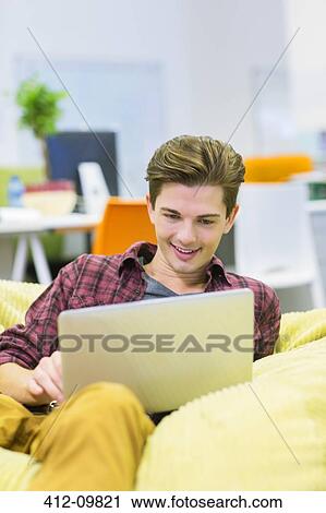 Stock Image - Businessman using laptop in bean bag chair in office. Fotosearch