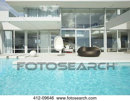 Chairs by swimming pool outside modern house View Large Photo Image Stock Photograph - Chairs by swimming pool outside modern house. Fotosearch