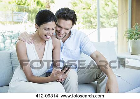 Couple using cell phone on sofa View Large Photo Image Picture - Couple using cell phone on sofa. Fotosearch