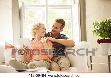 Couple using digital tablet on sofa View Large Photo Image Picture - Couple using digital tablet on sofa. Fotosearch