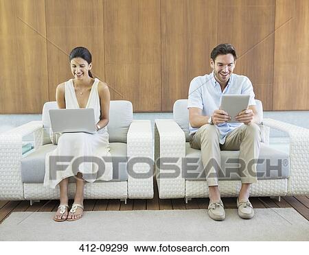 Couple using laptop and digital tablet in armchairs View Large Photo Image Stock Photo - Couple using laptop and digital tablet in armchairs. Fotosearch