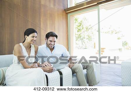 Couple using laptop on armchairs View Large Photo Image Stock Image - Couple using laptop on armchairs. Fotosearch