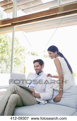 Stock Photo - Couple using laptop on sofa. Fotosearch