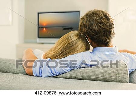 Couple watching television on sofa View Large Photo Image Stock Photograph - Couple watching television on sofa. Fotosearch