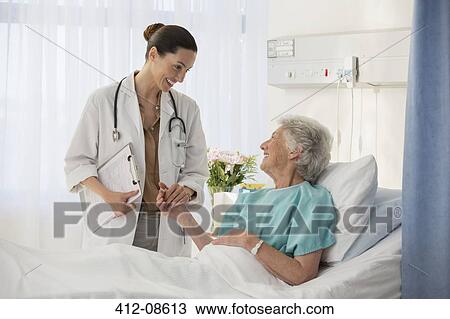 Stock Image - Doctor and senior patient talking in hospital room. Fotosearch