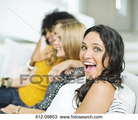 Stock Image - Enthusiastic woman on sofa with friends. Fotosearch