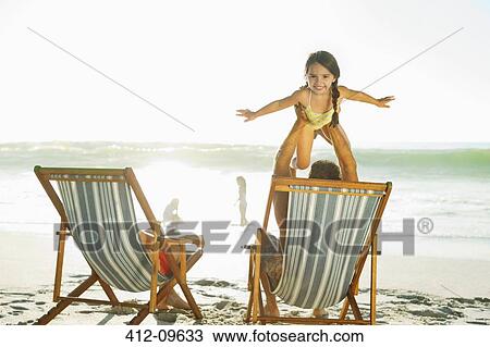 Stock Image - Father lifting daughter on beach. Fotosearch