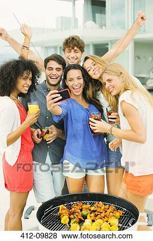 Stock Photo - Friends taking self-portrait with camera phone at barbecue. Fotosearch
