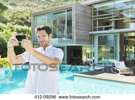 Stock Photograph - Man taking self-portrait with camera phone at poolside. Fotosearch