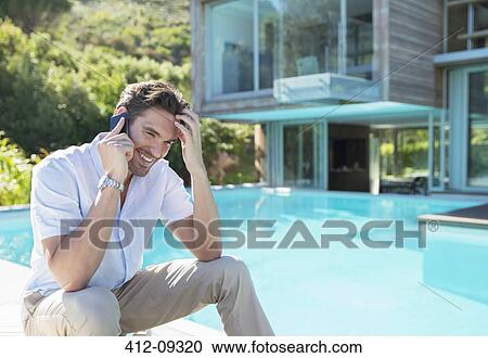 Stock Image - Man talking on cell phone at poolside. Fotosearch