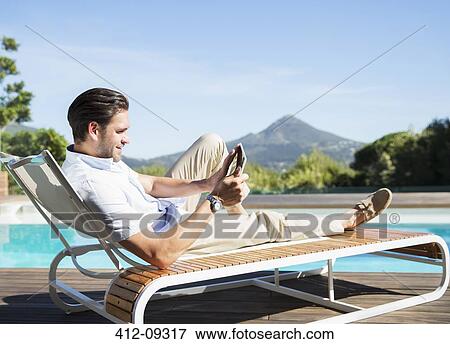 Man using digital tablet on lounge chair at poolside View Large Photo Image Stock Photo - Man using digital tablet on lounge chair at poolside. Fotosearch