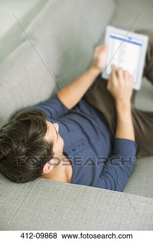 Man using digital tablet on sofa View Large Photo Image Stock Photo - Man using digital tablet on sofa. Fotosearch