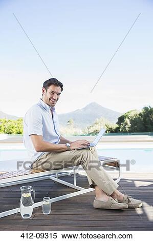Man using laptop on lounge chair at poolside View Large Photo Image Stock Photography - Man using laptop on lounge chair at poolside. Fotosearch