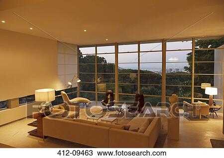 Stock Image - Modern living room overlooking trees and city in distance. Fotosearch