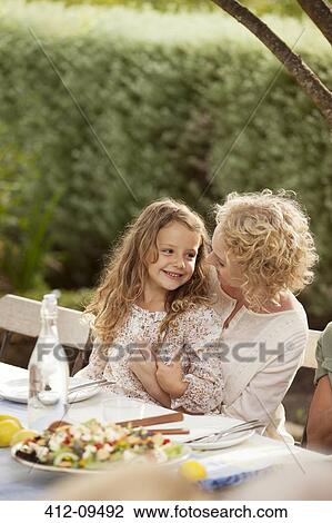 Stock Image - Mother and daughter sitting at table outdoors. Fotosearch