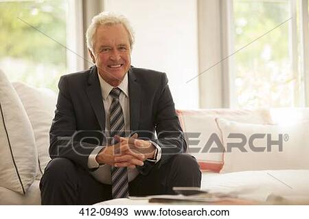 Stock Image - Portrait of smiling businessman on sofa. Fotosearch