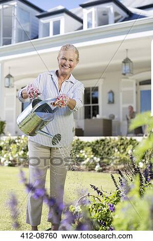 Portrait of smiling senior woman watering flowers in garden View Large Photo Image Stock Image - Portrait of smiling senior woman watering flowers in garden. Fotosearch