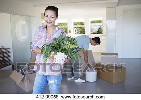 Portrait of smiling woman holding potted plant in new house View Large Photo Image Stock Photo - Portrait of smiling woman holding potted plant in new house. Fotosearch