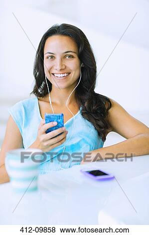 Portrait of smiling woman listening to mp3 player at table View Large Photo Image Stock Photo - Portrait of smiling woman listening to mp3 player at table. Fotosearch