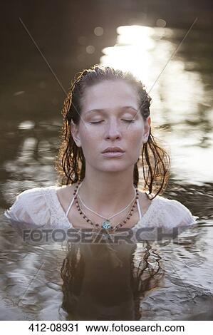 Stock Image - Serene woman with eyes closed in river. Fotosearch