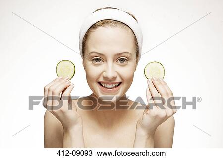 Stock Image - Smiling woman holding cucumber slices. Fotosearch
