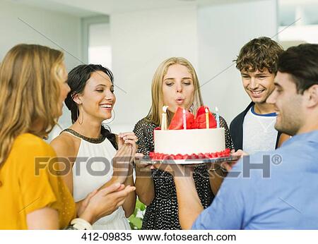 Stock Photography - Woman blowing out candles on birthday cake. Fotosearch