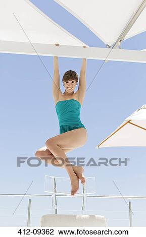 Stock Image - Woman hanging from deck beam. Fotosearch