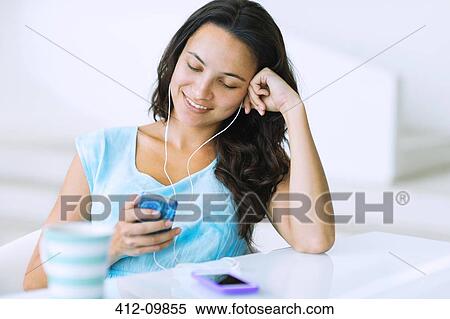 Stock Photography - Woman listening to mp3 player at table. Fotosearch