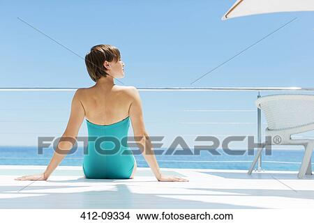 Woman relaxing poolside with ocean in background View Large Photo Image Picture - Woman relaxing poolside with ocean in background. Fotosearch