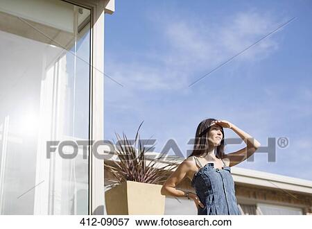 Woman shielding eyes outside modern house View Large Photo Image Stock Photo - Woman shielding eyes outside modern house. Fotosearch
