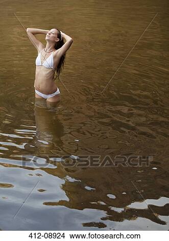 Picture - Woman standing with hands in hair in river. Fotosearch