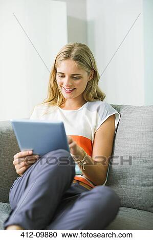 Stock Image - Woman using digital tablet on sofa. Fotosearch