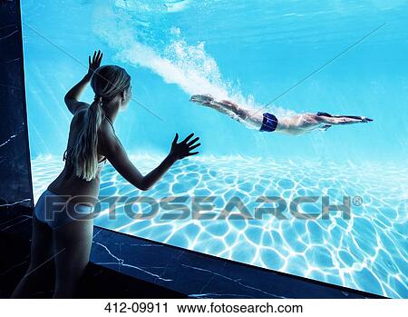 Stock Image - Woman watching boyfriend underwater in swimming pool. Fotosearch